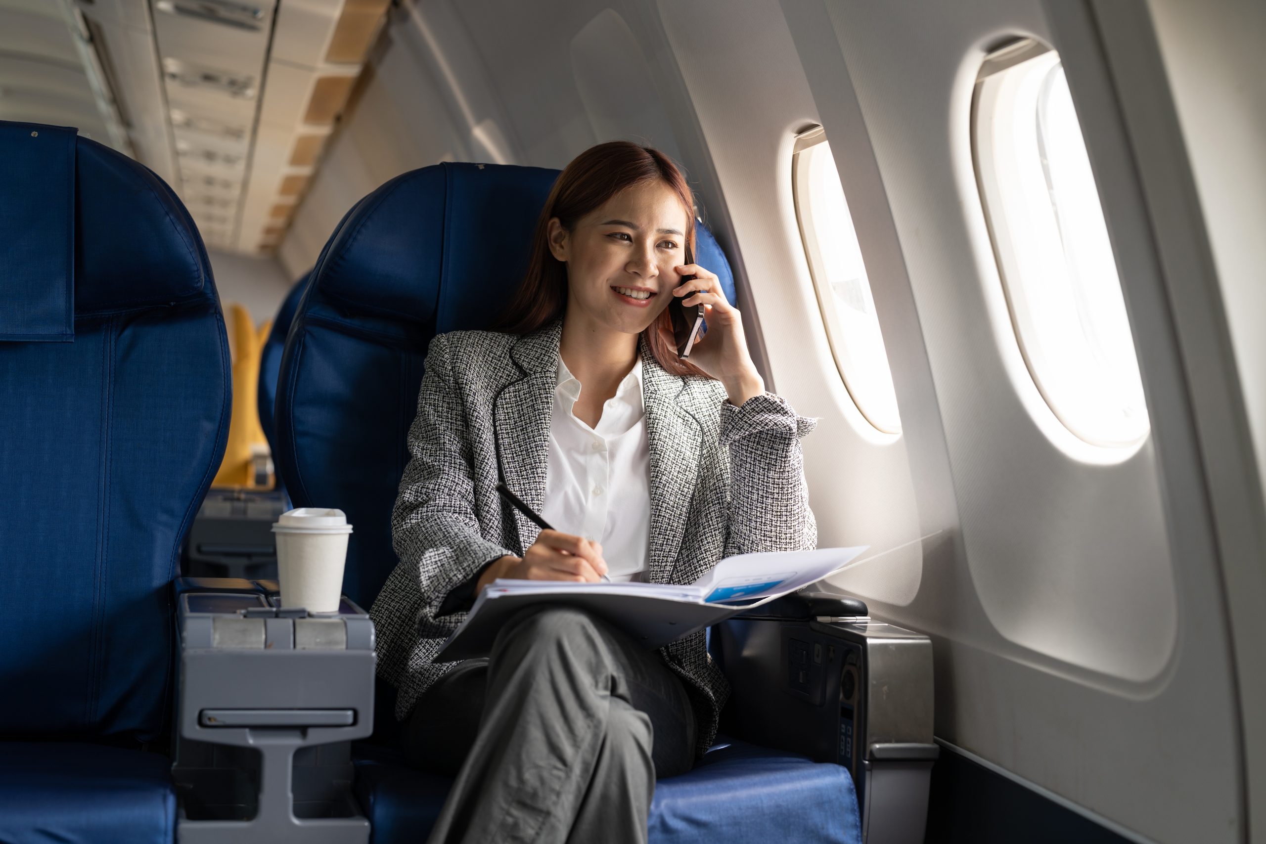 Young attractive and successful business asian woman talking on the phone and working while sitting in the chair of his private business plane